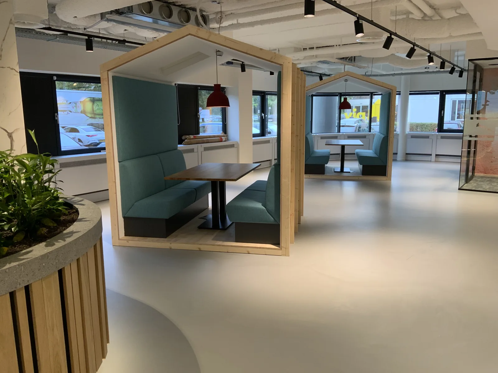 Light concrete-look resin floor in an open-plan office with timber meeting pods and plants